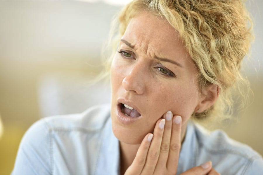 A blonde woman holds her jaw in pain.