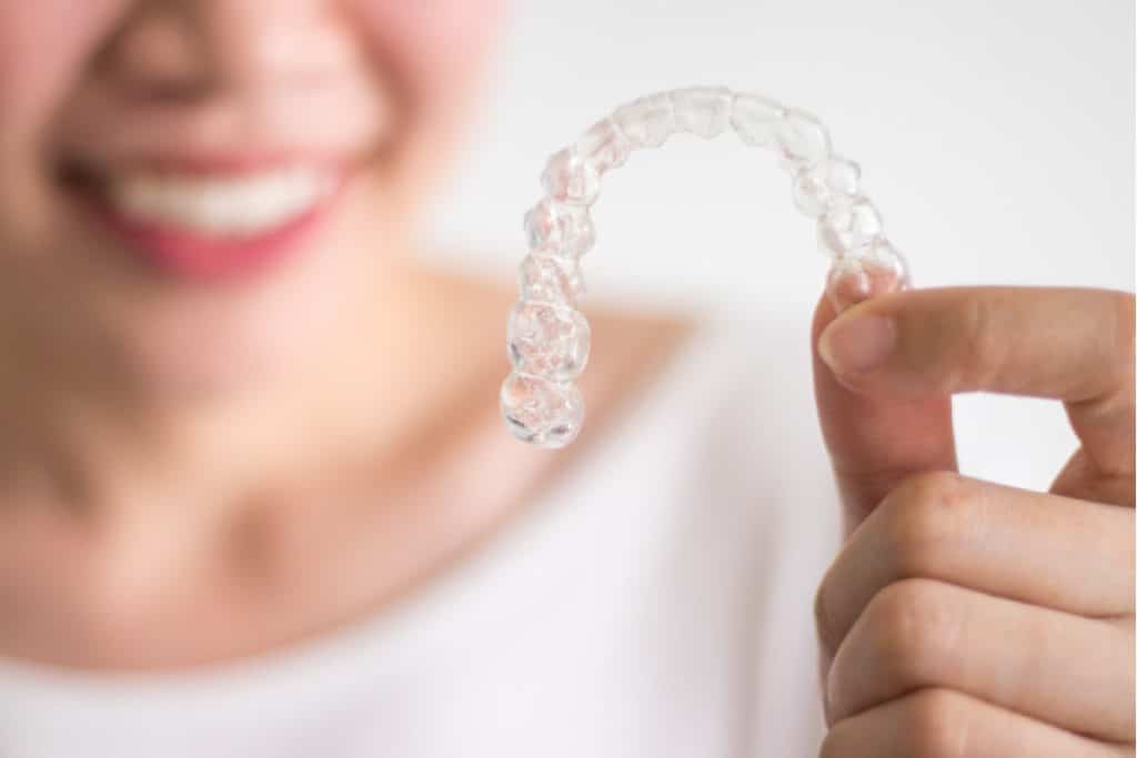 Blurred image of a woman holding a clear aligner in focus.