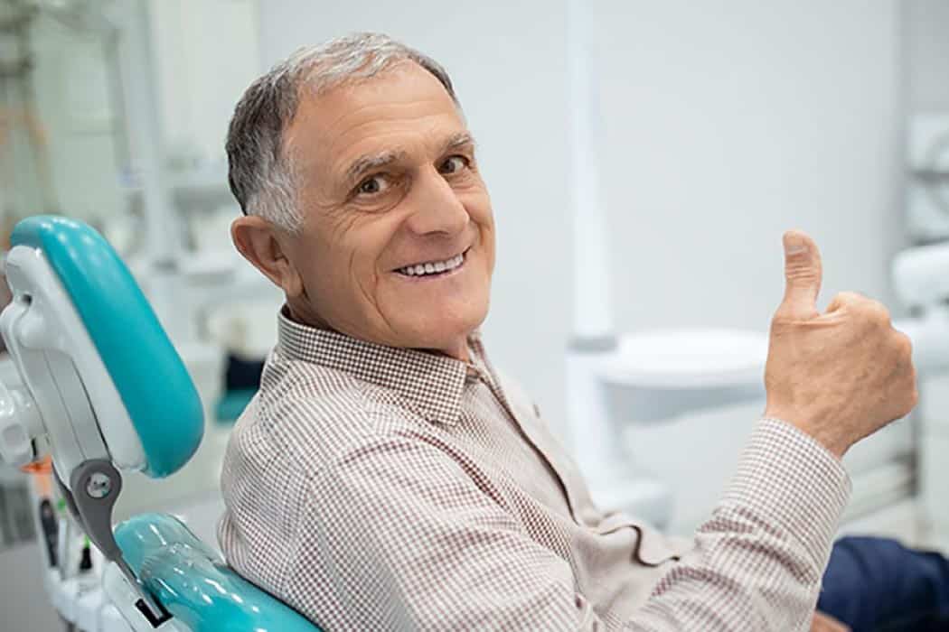 Smiling elderly man giving the thumbs up sign from the dental chair.
