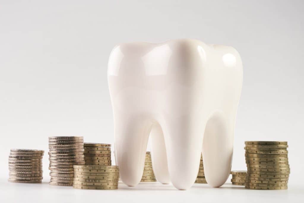 A model of a tooth with stacks of coins surrounding it indicating financial choices related to dental care.