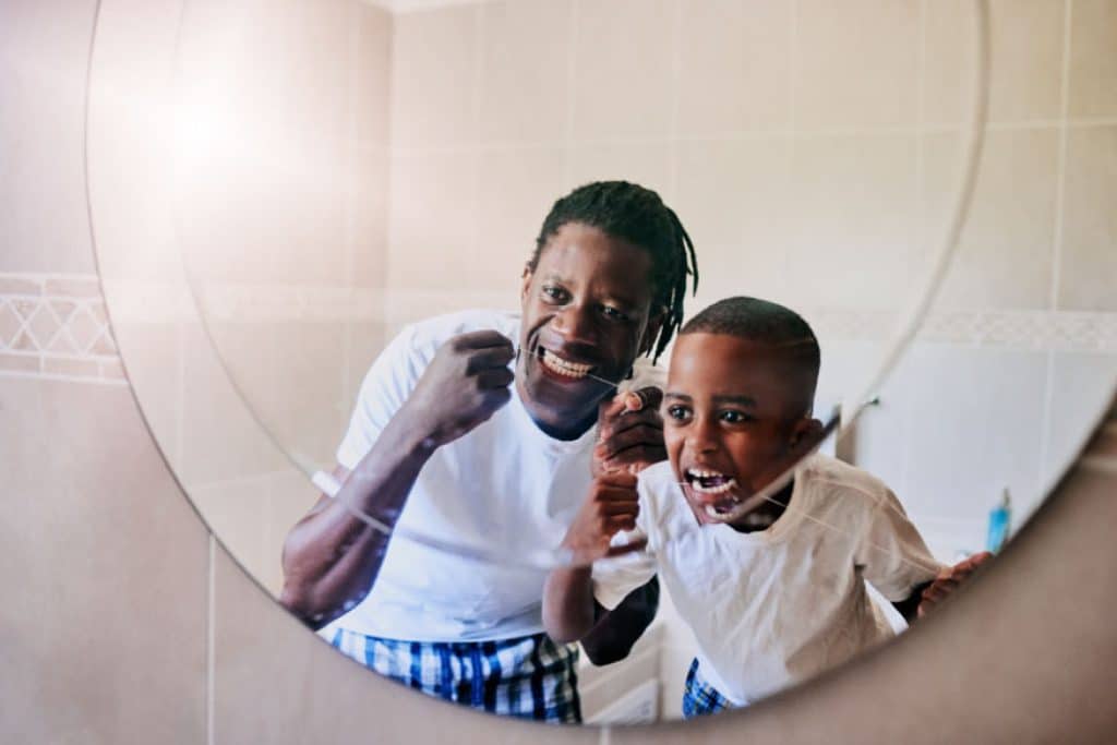 man and young boy floss teeth together