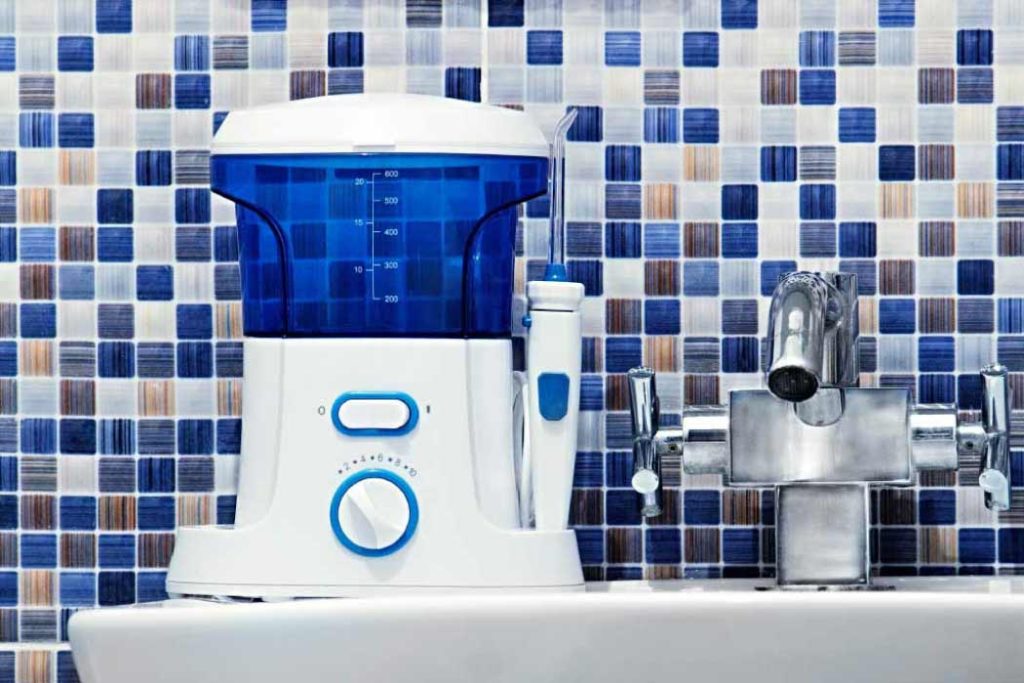 water flosser sitting on a bathroom shelf with blue and white tiles
